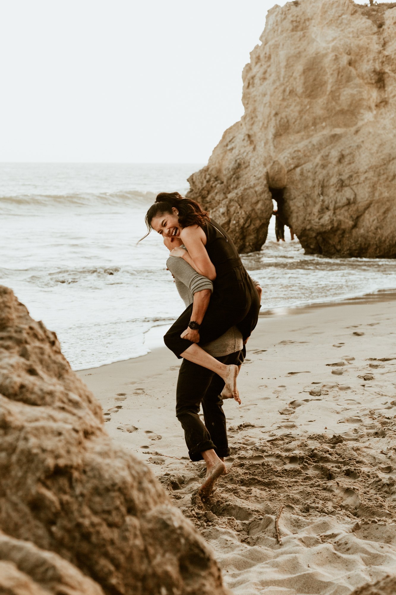 A couple playing on the beach, one carrying the other