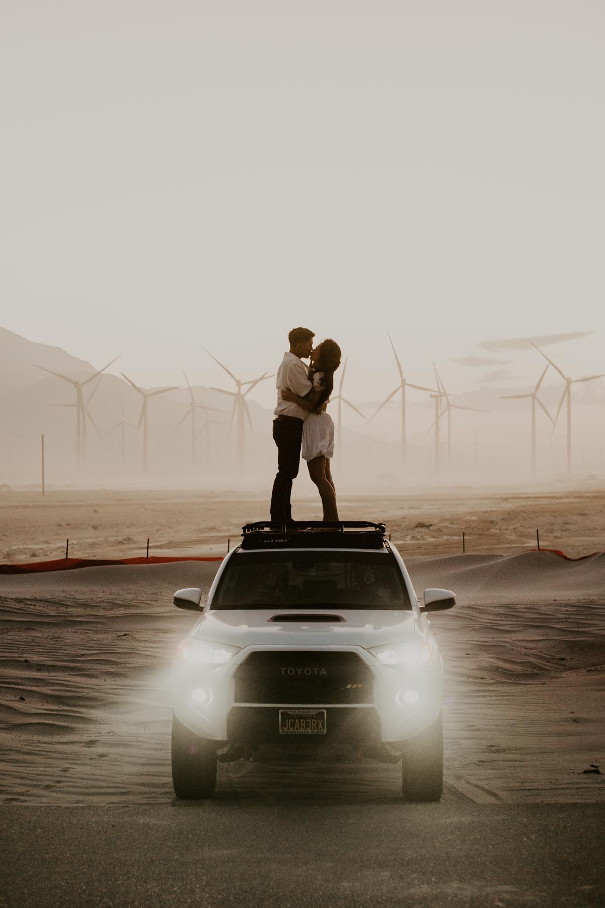 A couple kissing on the roof of a truck among desert windmills