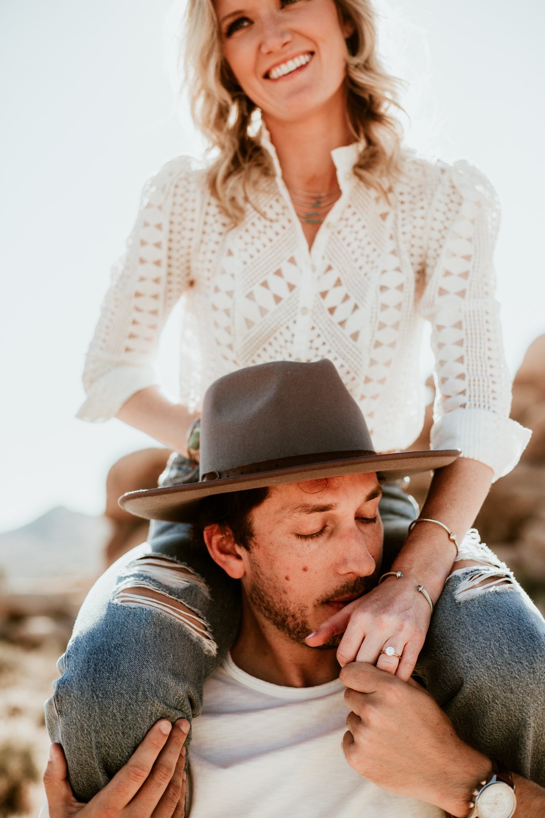 One partner sitting on the other’s shoulders, both laughing in the desert