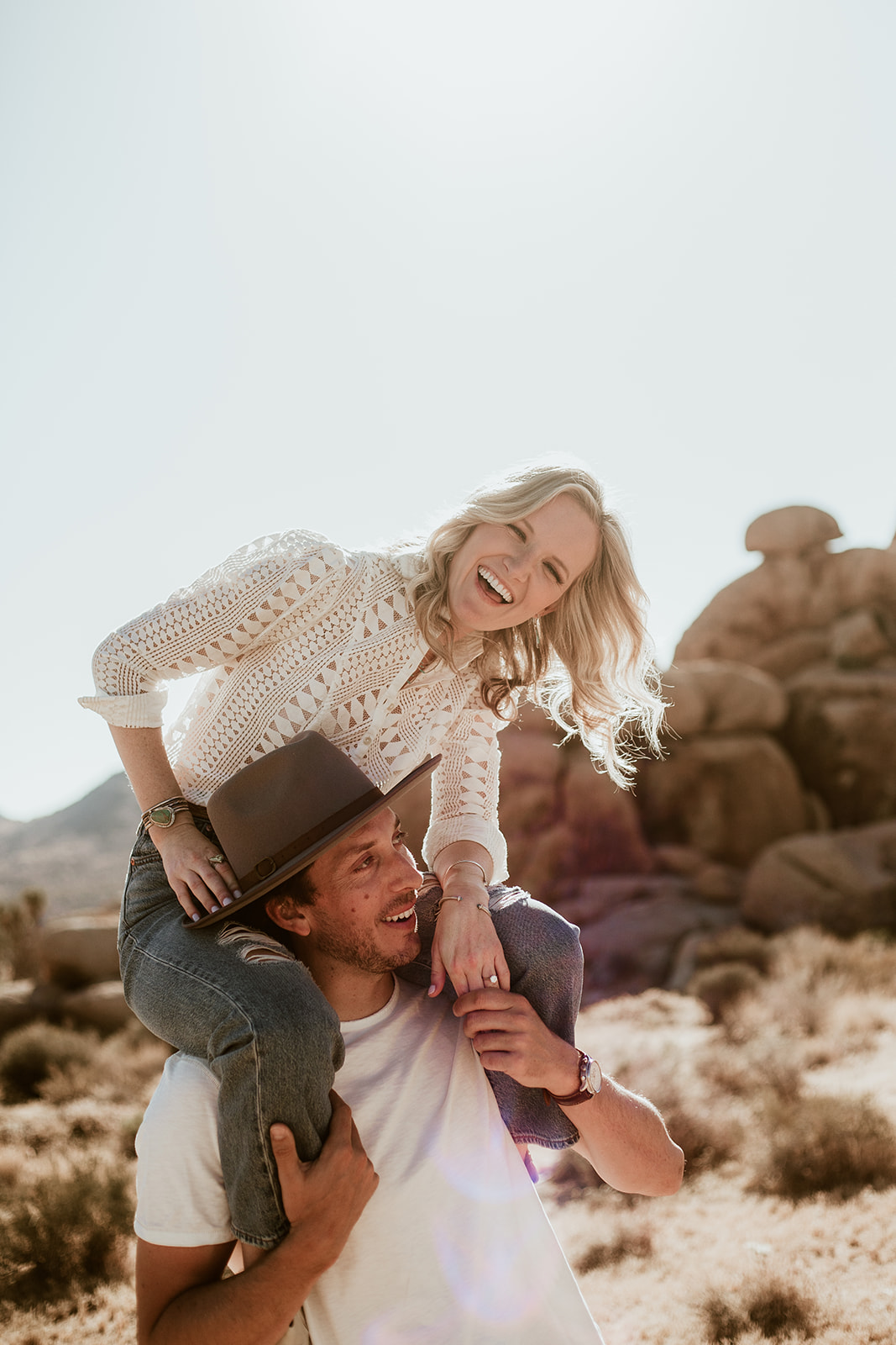 A couple laughing in a piggyback ride among the Joshua Tree rocks