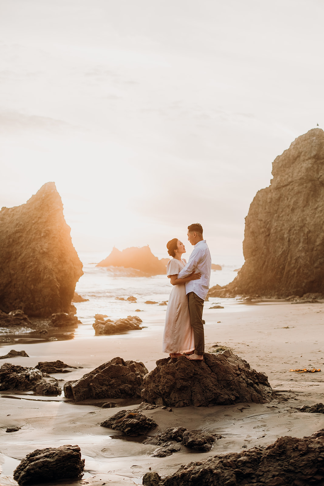 A couple standing on a rock at El Matador beach at sunset