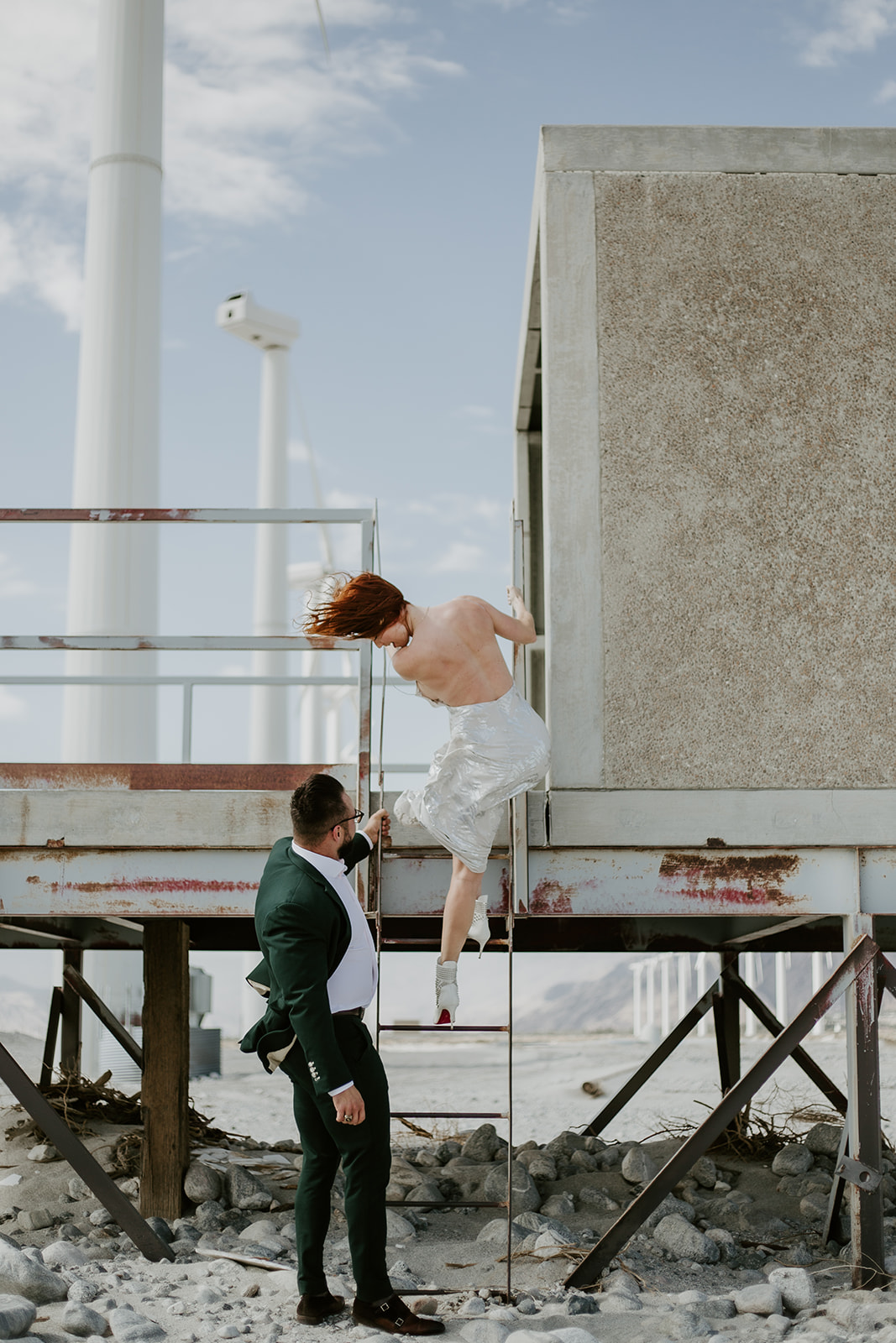 A couple climbing a ladder beside the desert windmills