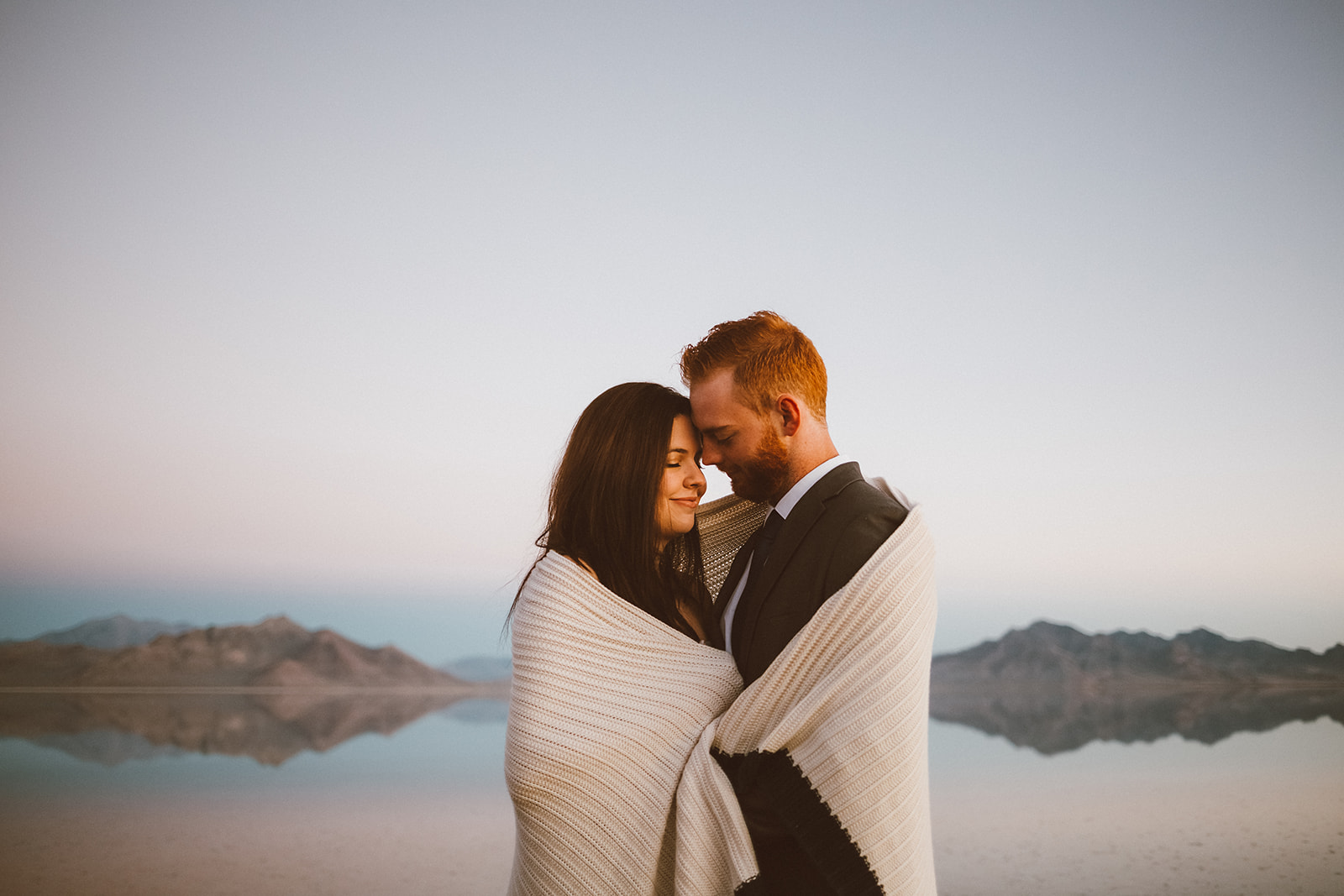 A couple wrapped in a blanket on the salt flats at dusk